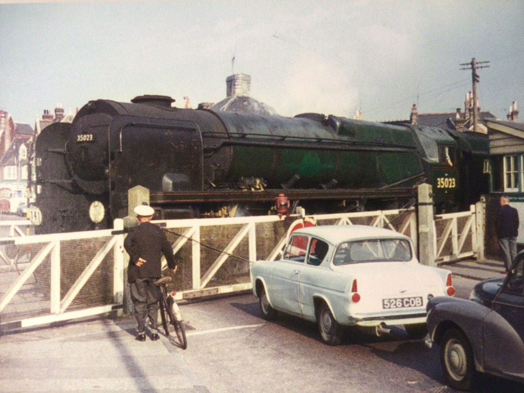 Alex Coomber on Train Siding: An evocative 1960s period photo with Pedestrians, A cyclist, A Ford Anglia, A Morris Minor and in the background is a bus all held
up by...